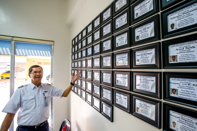 Instruktur AAA Academy di depan dinding sertifikat dan pencapaian pelatihan penerbangan