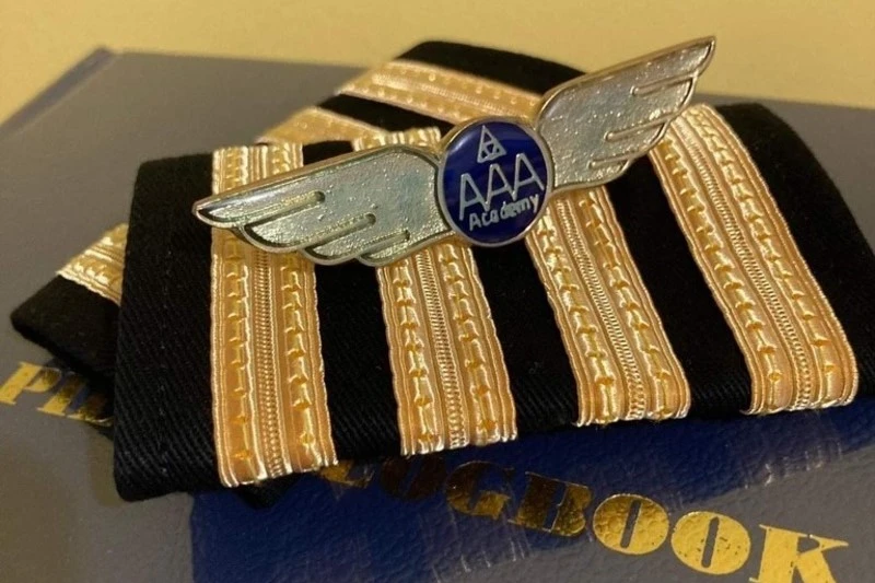 Lencana sayap AAA Academy dan tanda pangkat pilot diletakkan di atas buku log penerbangan.